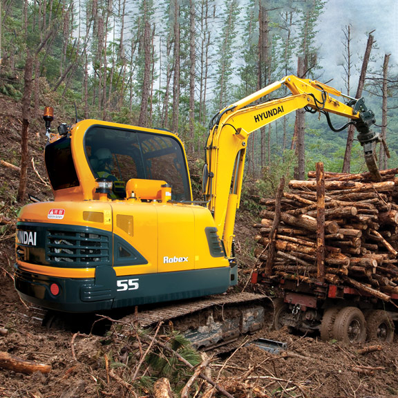 Compacte graafmachine R55-9A verplaatst boomstammen in een bos met behulp van een grijperhulpstuk.