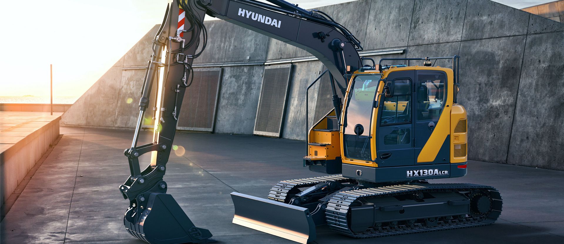 HX130A LCR excavator parked in front of a large wall at sunset