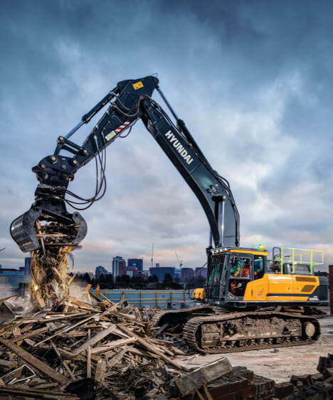 Pelle sur chenilles HD Hyundai HX520A L sur un chantier de démolition utilisant l'accessoire de préhension