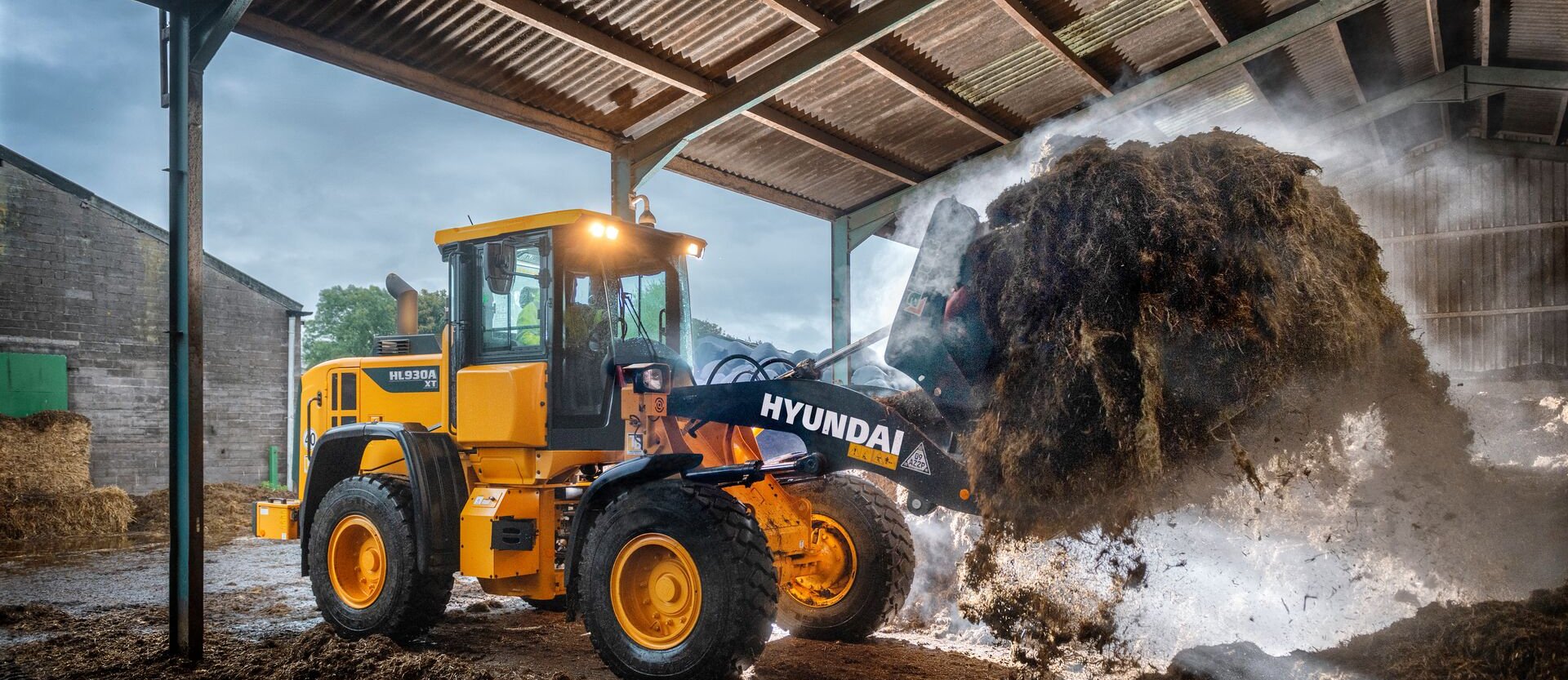 Chargeur sur pneus HD Hyundai HL930A déplaçant du matériel agricole dans une ferme