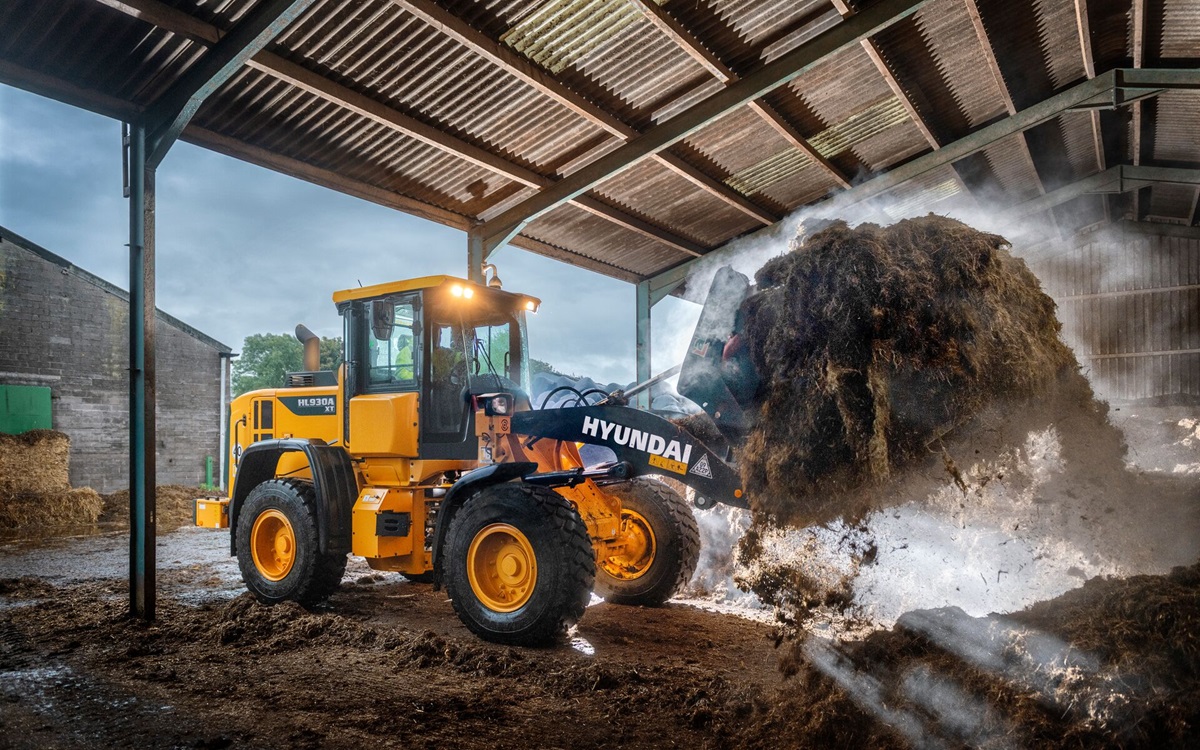Chargeur sur pneus HD Hyundai HL930A déplaçant du matériel agricole dans une ferme