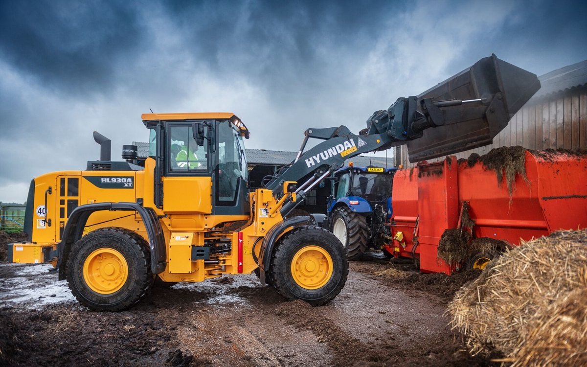 Chargeur sur pneus HD Hyundai HL930A déchargeant du matériel agricole dans une ferme