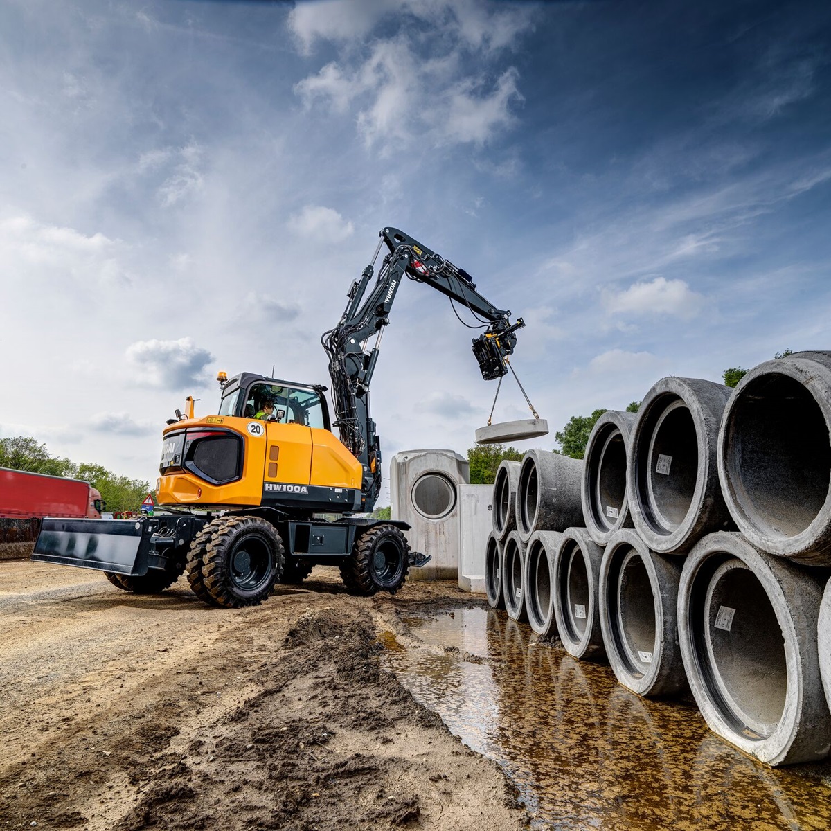 Een mobiele graafmachines op wielen verplaatst grote buizen op een bouwterrein